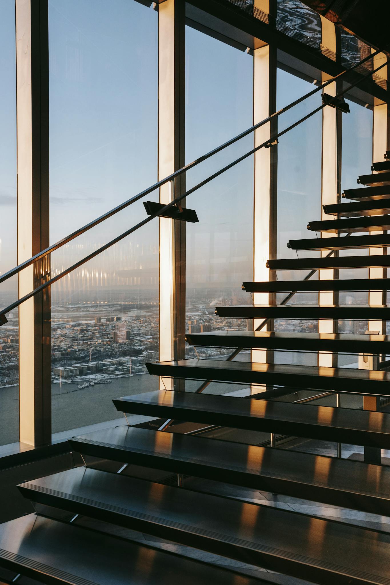 Stairway with metal railing located in contemporary business center with bright sunlight near glass wall overlooking modern city with buildings